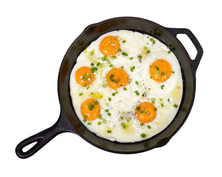 Fried eggs on cast iron skillet with salt, pepper and green onion isolated on white background