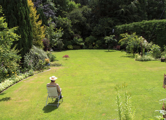 A lone man in straw hat sitting  on a deck chair relaxing in large garden