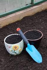 Ceramic flowerpots filled with the fresh soil for planting and a garden trowel in the polycarbonate greenhouse prepared for wintering