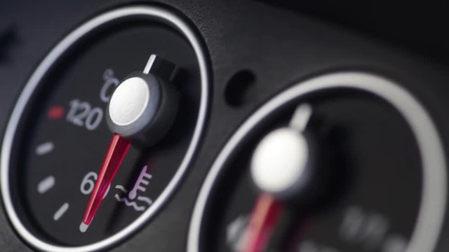 Color close up footage of a car's coolant temperature gauge and a red light blinking.