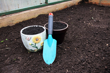 Ceramic flowerpots filled with the fresh soil for planting and a garden trowel in the polycarbonate greenhouse prepared for wintering