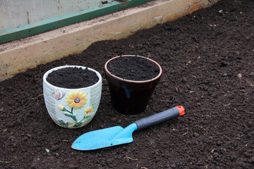 Ceramic flowerpots filled with the fresh soil for planting and a garden trowel in the polycarbonate greenhouse prepared for wintering