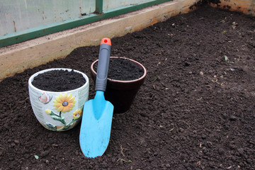 Ceramic flowerpots filled with the fresh soil for planting and a garden trowel in the polycarbonate greenhouse prepared for wintering