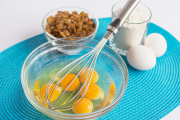glass bowl with chicken eggs and whisk, set of products for muff