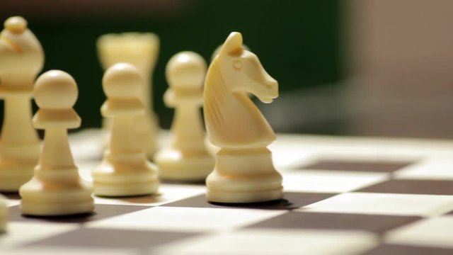 Panning shot of a chess board with a hand moving the white horse.