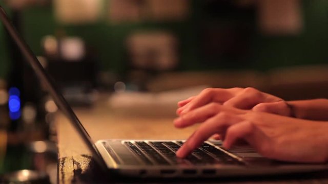 Moving shot of the hands of a woman typing at a laptop.