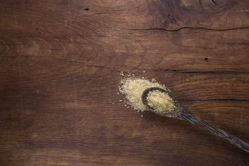  Spoon with brown sugar, on old wooden background.