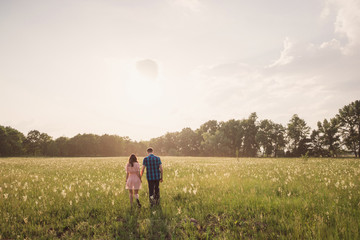 young couple walking in the field with flowers in sunlight - Powered by Adobe
