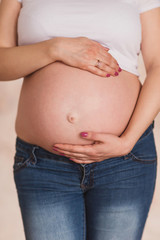 pregnant woman in jeans and white t-shirt holding her hands on her belly