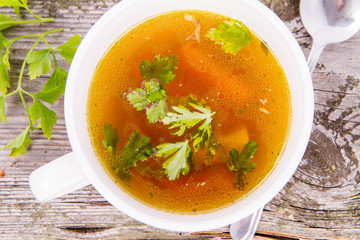Chicken soup with carrots and parsley on wooden background