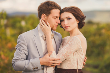 Romantic and stylish caucasian couple standing in the beautiful vineyard at sunset. Love, relationships, romance, happiness concept.