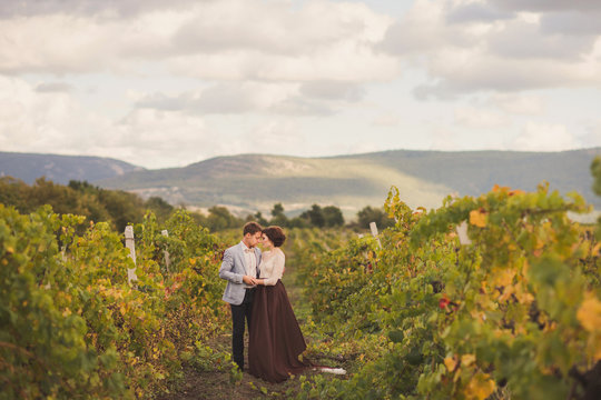 Romantic and stylish caucasian couple standing in the beautiful vineyard at sunset. Love, relationships, romance, happiness concept.