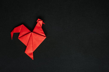Red fire paper folded rooster handmade origami craft on black background. Nice natural holiday greeting card template. Empty space for text, copy, lettering.