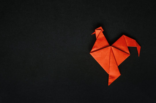 Red fire paper folded rooster handmade origami craft on black background. Nice natural holiday greeting card template. Empty space for text, copy, lettering.
