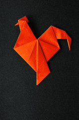 Red fire paper folded rooster handmade origami craft on black background. Nice natural holiday...