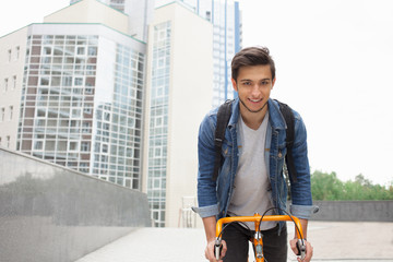 The guy goes to town on a bicycle in  blue jeans jacket .  young man  an orange fix bike