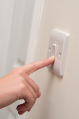 Finger Presses Light Switch on Wall Next to Door