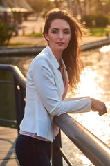 Beautiful young woman outside city urban walking park gazing over canal sunset