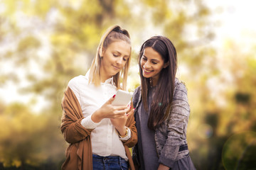 Young girls in the park looking at mobile.