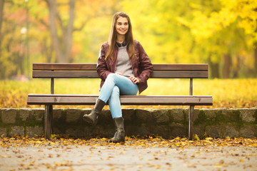 Young woman is sitting on a bench in a park on an Autumn day. She is wailting for someone