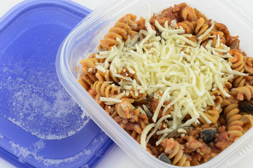 Close up of frozen casserole portion in plastic container on white background