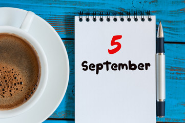 September 5th. Day 5 of month, coffee cup with loose-leaf calendar on freelancer workplace...