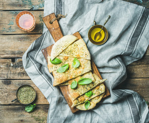 Homemade Italian focaccia flatbread cut into pieces with herbs, fresh basil leaves, olive oil and...