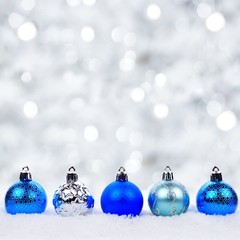 Blue and silver Christmas ornaments in snow with twinkling silver background
