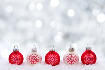 Red and white Christmas ornaments with snowflakes in snow with twinkling silver background