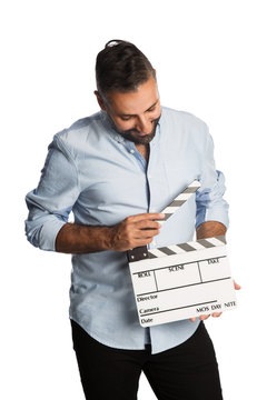 An attractive man wearing a light blue shirt standing against a white background holding a movie slate.