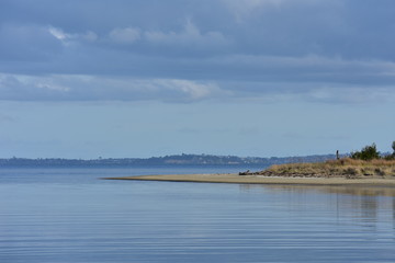 Mirror like sea around sandspit on very calm day.