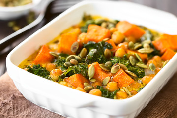 Baked pumpkin, kale and chickpea casserole with pumpkin seeds on top in casserole dish, photographed with natural light (Selective Focus, Focus one third into the image)