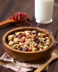 Crunchy oatmeal cereal with almond and dried goji berries and cranberries in wooden bowl, photographed with natural light (Selective Focus, Focus in the middle of the bowl)