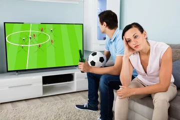 Foto op Canvas Sad Woman Sitting Beside A Man Busy Watching Football © Andrey Popov