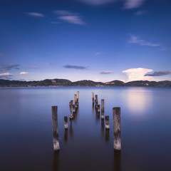 Obrazy na Szkle  Drewniane molo lub molo pozostaje na niebieskim jeziorze o zachodzie słońca. Włochy