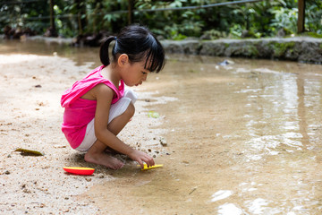 Asian Chinese little girl playing toy boat at creek