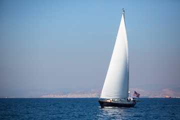 Sailing yacht with white sails in the fog in the sea near the coast.