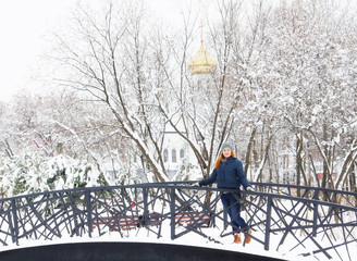 Happy beautiful girl has a rest on the bridge in winter park
