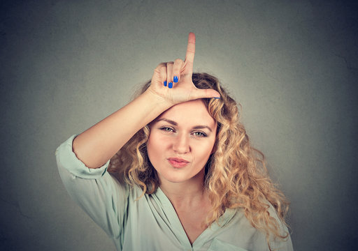 young unhappy woman giving loser sign on forehead