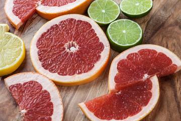 Fototapeta na wymiar Slices of red grapefruit, lemon, and lime on acacia chopping board closeup