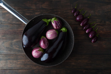 Eggplant varieties arranged on frying pan and wooden table. Top view.