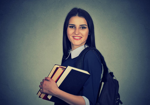Smiling student carrying backpack and holding stack of books