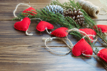 Christmas or New Year background. Natural fir tree brunch and cones with felt heart garland on wooden rustic table. Winter holidays concept. Copy space.