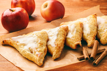 Puff pastries with apples and cinnamon on brown background.
