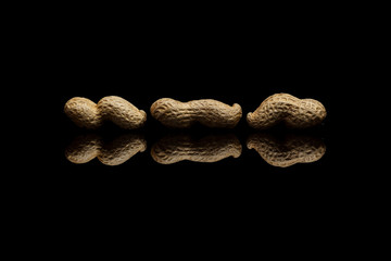 Three whole peanuts isolated on black reflective background