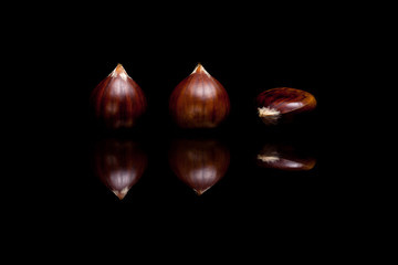 Three brown chestnuts isolated on black reflective background