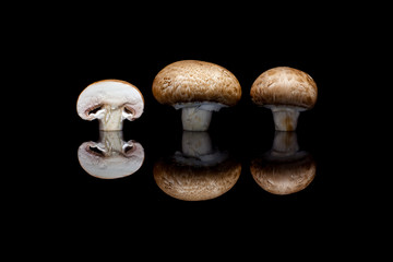 Two whole and one cut brown champignons in row isolated on black