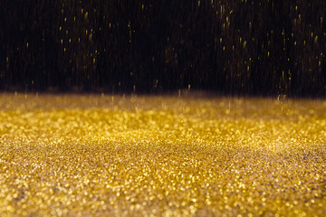 Golden glitter sand rain texture on black, abstract background.