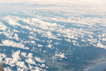 Cloudscape view with mountain above white clouds and blue sky from airplane