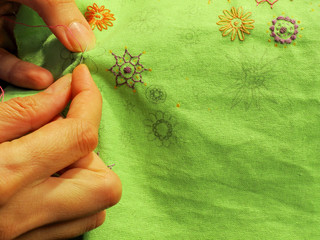 Hands girls embroider abstract patterns of flowers on a green cloth. Embroidery. Women's hobby. Creative work